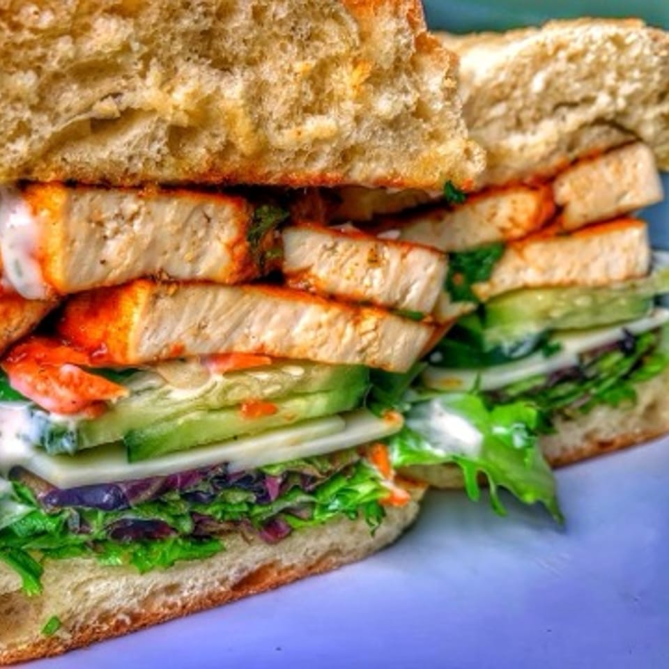 A vegan sandwich with tofu, lettuce, cucumbers, and sauce on toasted bread.