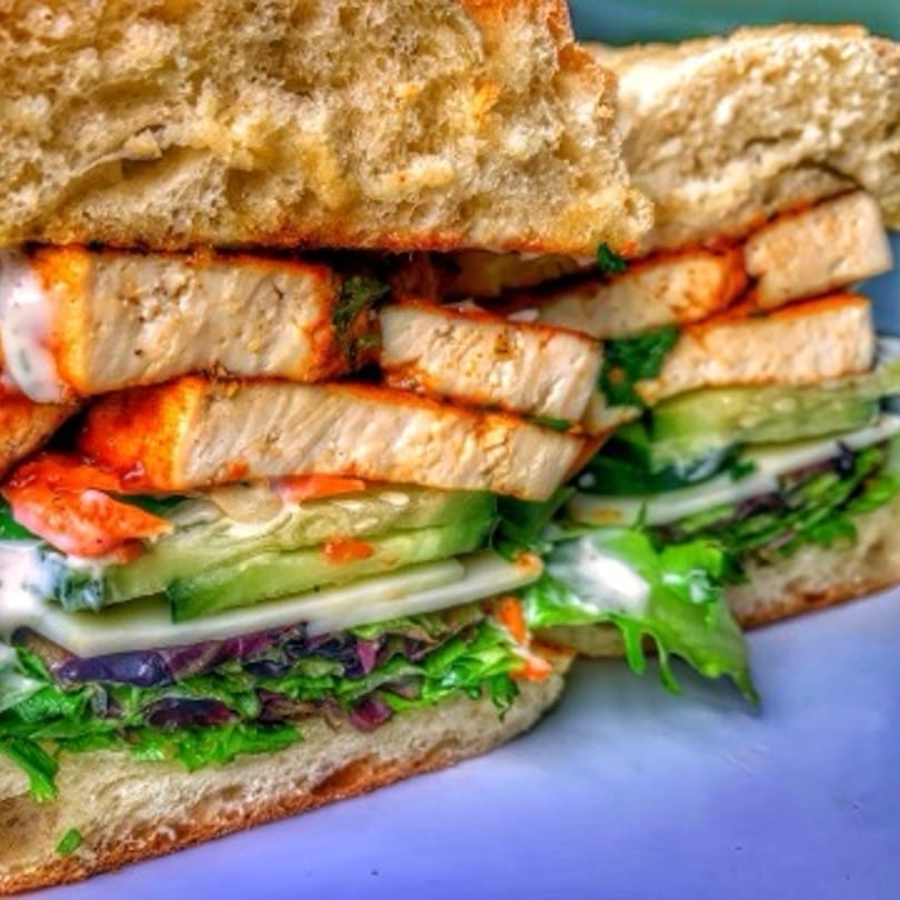 A vegan sandwich with tofu, lettuce, cucumbers, and sauce on toasted bread.